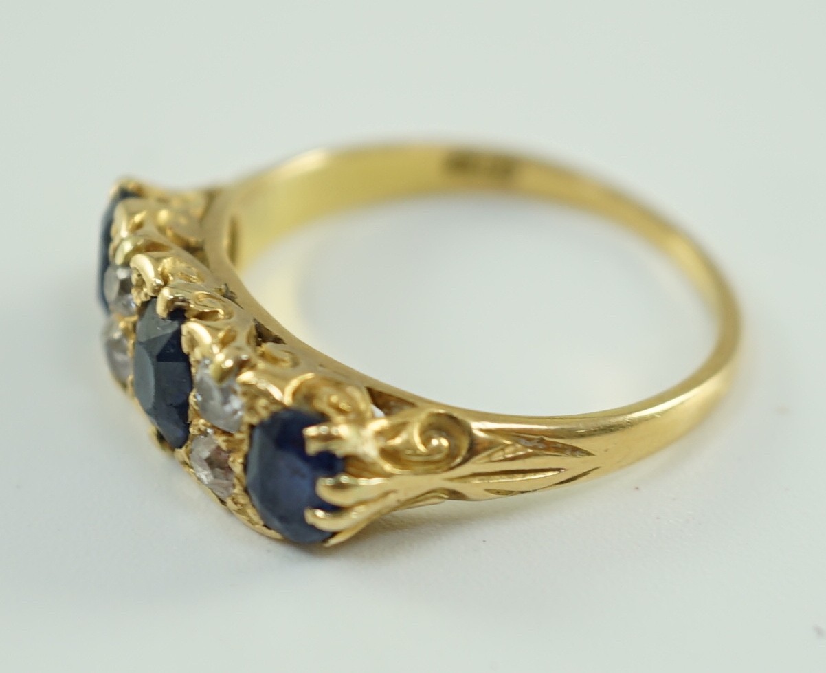 An early 20th century 18ct gold, three stone oval cut sapphire and four stone diamond spacer set half hoop ring